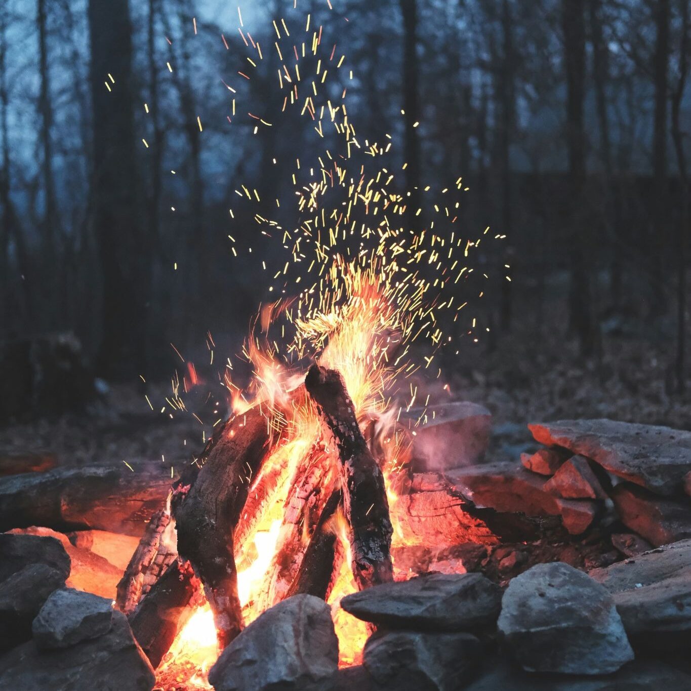 A warm and cozy campfire burns surrounded by rocks. Sparks fly upwards into the evening air.